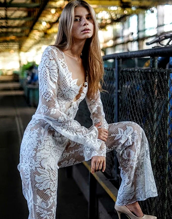 Woman wearing a white lace outfit sitting on a bench in an urban setting.