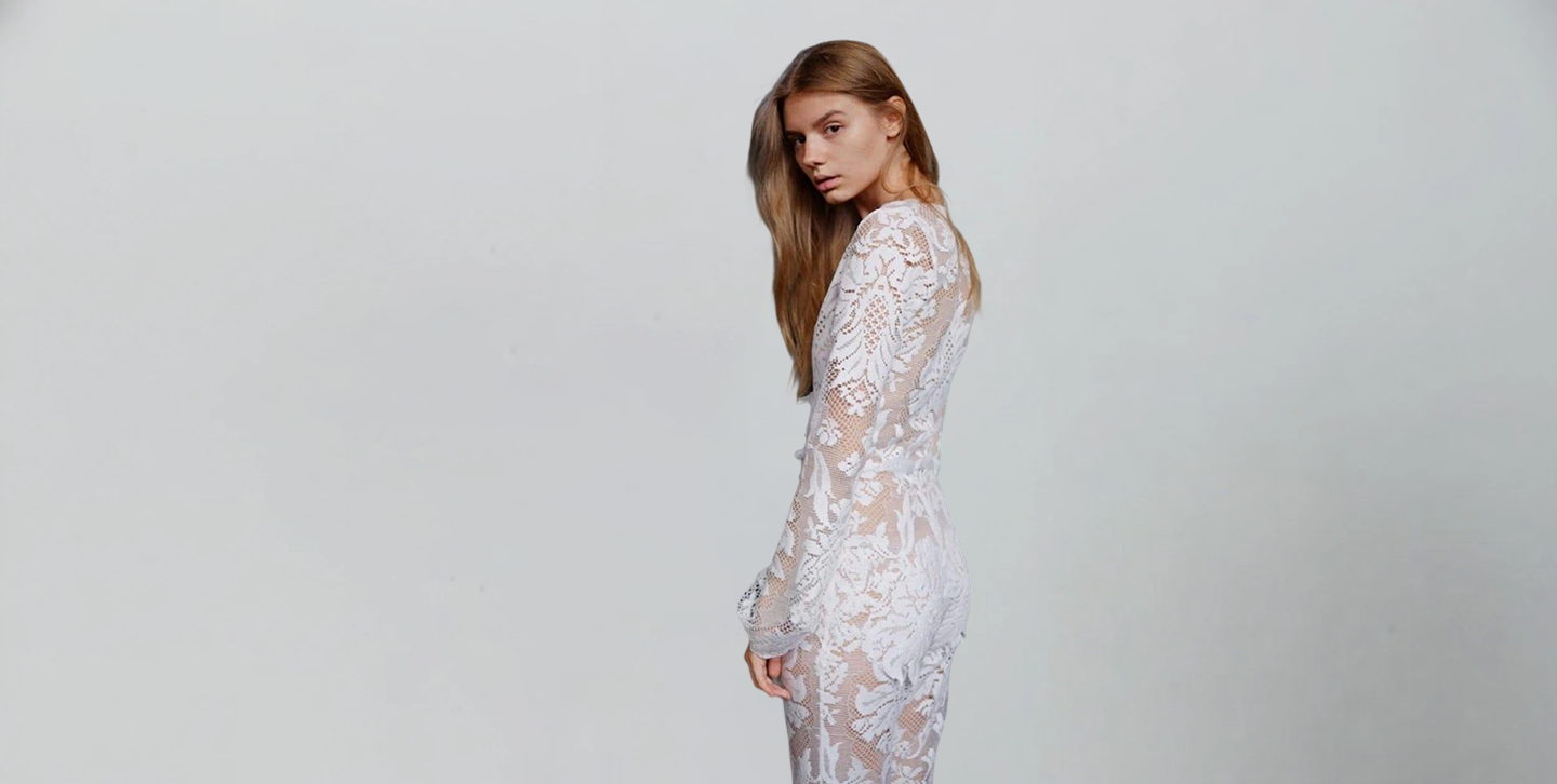 Woman wearing a white lace Jumpsuit against a plain background