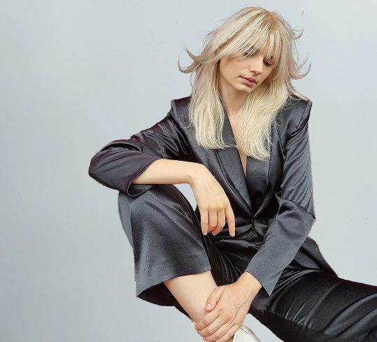 Person wearing a dark gray satin outfit sitting against a light gray background