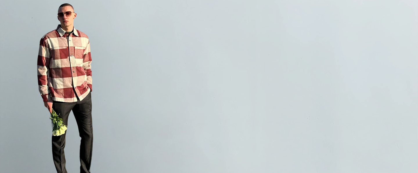 Man wearing a Luxury shirt and sunglasses holding a bottle against a plain background