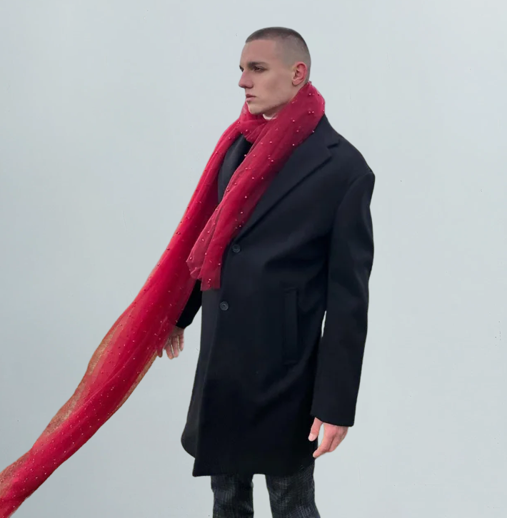 Man wearing a black coat and red scarf on a light gray background