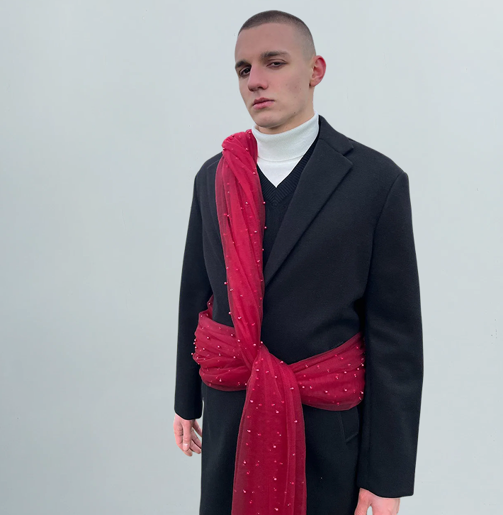 Person wearing a black coat with a red scarf against a plain background