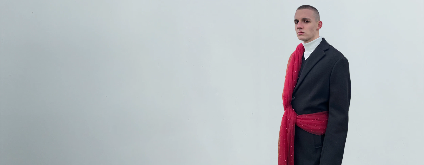 Man wearing a black coat with a red scarf against a plain background