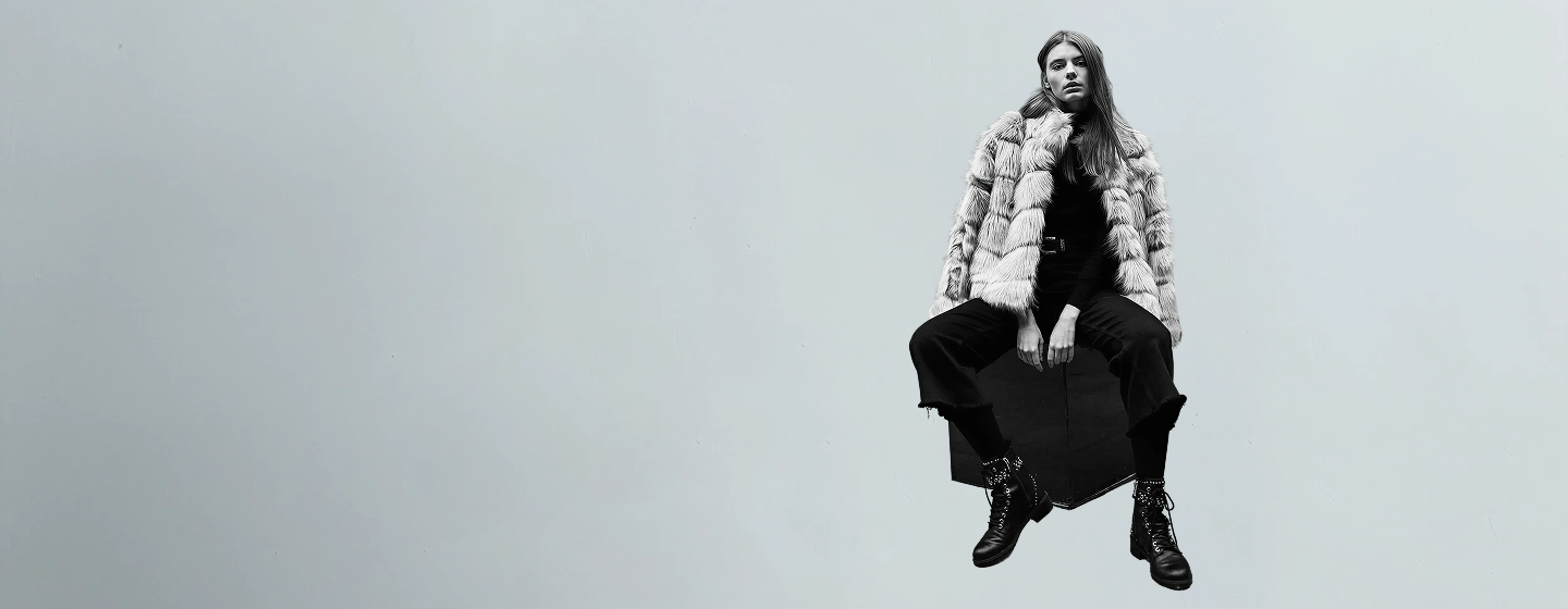 Person wearing a checkered jacket and black coat against a gray background